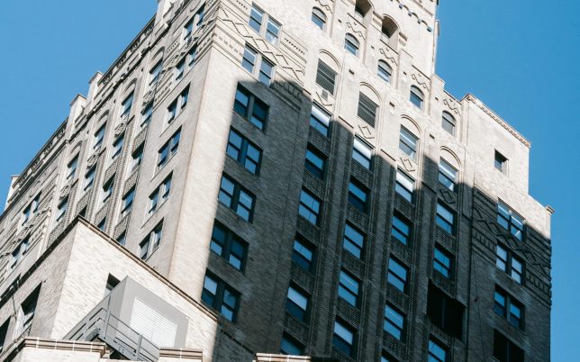 From below of old multistory building with stone decorative elements located against blue sky